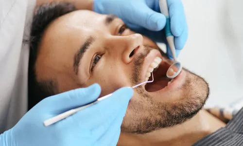 Smiling young man sitting in dentist chair while doctor examining his teeth